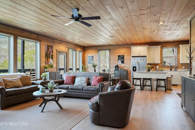 living room featuring wood walls, sink, light hardwood / wood-style floors, ceiling fan, and wood ceiling