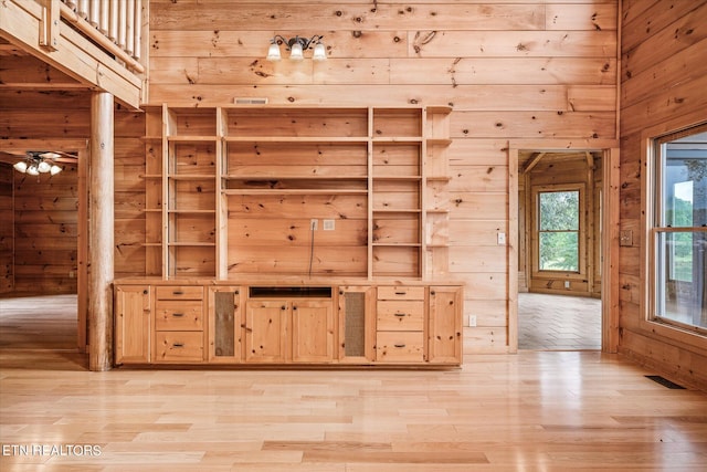 interior space with ceiling fan, wooden walls, light brown cabinetry, and light hardwood / wood-style floors