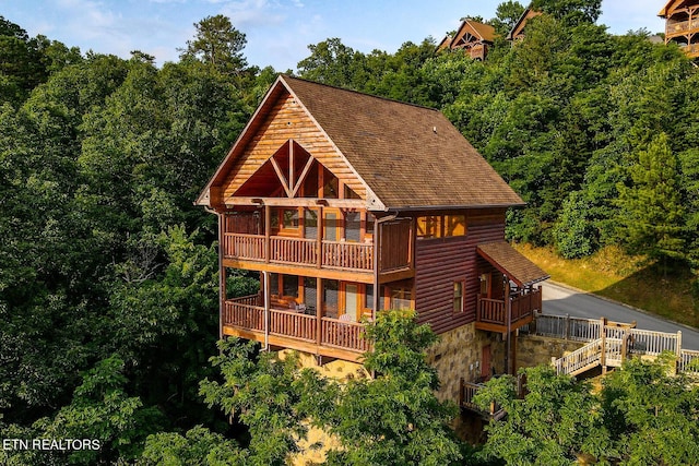 back of property featuring stone siding, a forest view, and roof with shingles