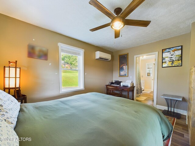 bedroom with ceiling fan, wood-type flooring, a wall mounted AC, ensuite bathroom, and a textured ceiling