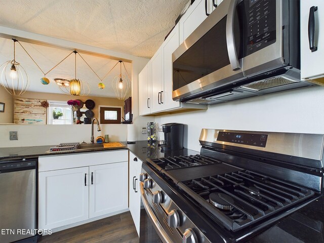 kitchen featuring appliances with stainless steel finishes, white cabinetry, dark hardwood / wood-style floors, a textured ceiling, and hanging light fixtures