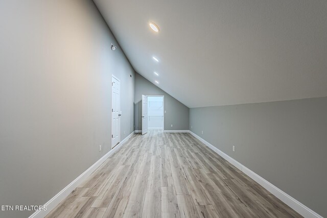 bonus room with baseboards, light wood-style flooring, and vaulted ceiling