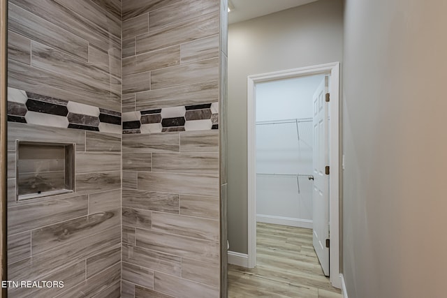 bathroom with baseboards, wood finished floors, and a tile shower