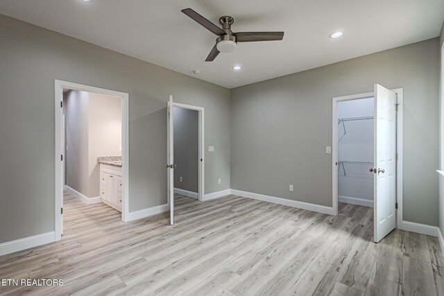 unfurnished bedroom with ceiling fan, a walk in closet, ensuite bath, and light hardwood / wood-style flooring