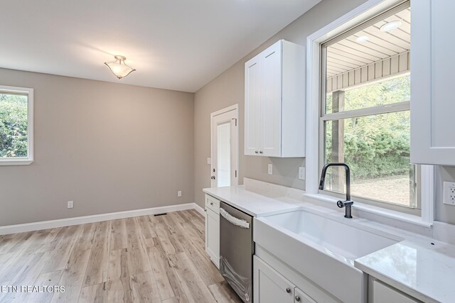 kitchen with baseboards, light countertops, stainless steel dishwasher, white cabinets, and a sink