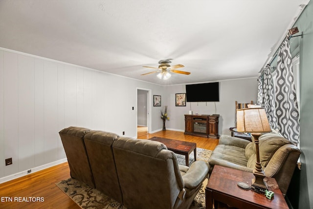 living room featuring wood walls, ornamental molding, light hardwood / wood-style flooring, and ceiling fan