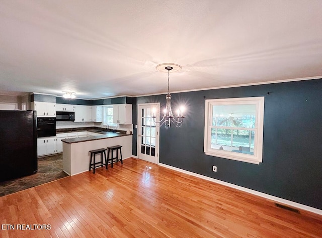 kitchen with kitchen peninsula, white cabinetry, light hardwood / wood-style flooring, black appliances, and decorative light fixtures