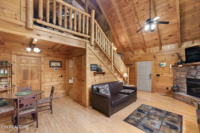 living room with ceiling fan, wood walls, light hardwood / wood-style flooring, and a stone fireplace