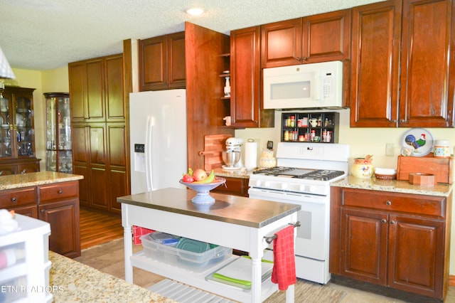 kitchen featuring a textured ceiling, light hardwood / wood-style floors, light stone countertops, and white appliances