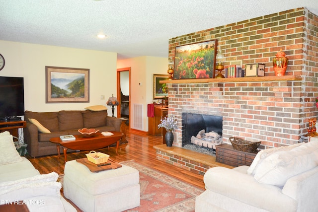 living room featuring a fireplace, brick wall, a textured ceiling, and hardwood / wood-style flooring