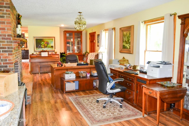 office featuring light hardwood / wood-style flooring, a chandelier, brick wall, a textured ceiling, and a brick fireplace