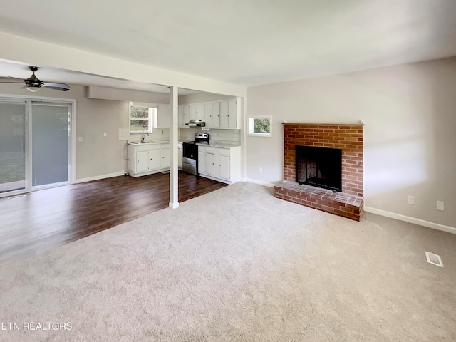 unfurnished living room featuring a fireplace, ceiling fan, dark carpet, and a healthy amount of sunlight