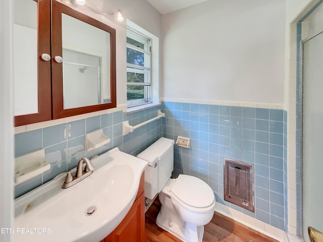 bathroom with a shower with door, toilet, vanity, wood-type flooring, and tile walls