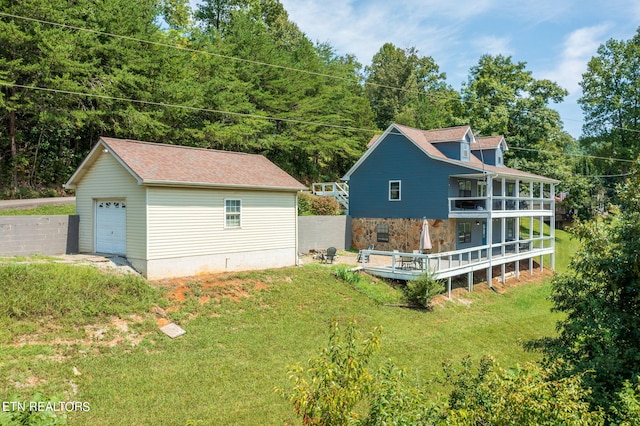 back of property with a balcony, a lawn, a garage, a deck, and an outbuilding