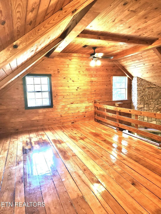 bonus room featuring plenty of natural light, lofted ceiling with beams, wooden walls, and hardwood / wood-style flooring