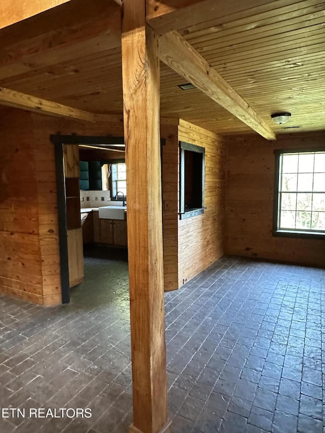 interior space with wooden walls, wood ceiling, brick floor, and a sink
