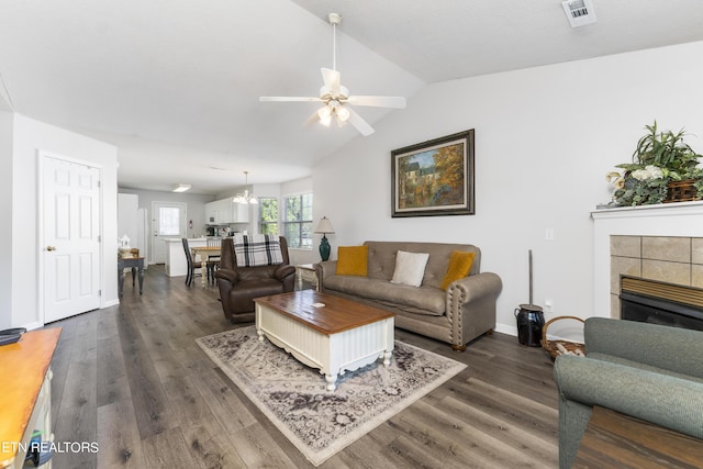 living room featuring ceiling fan with notable chandelier, lofted ceiling, dark wood-type flooring, and a tile fireplace