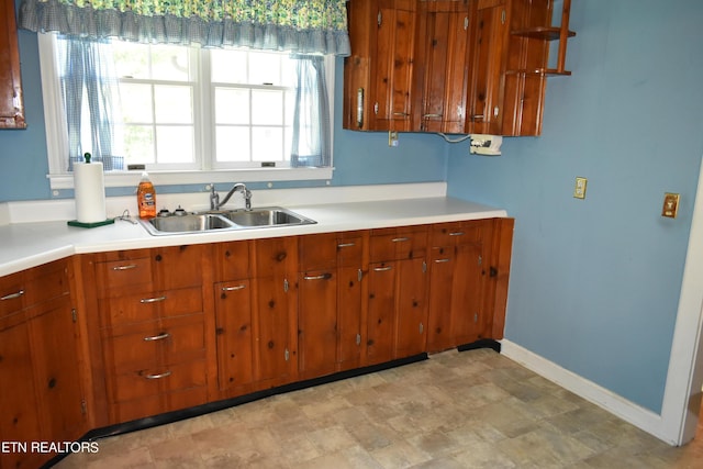 kitchen with baseboards, light countertops, a sink, and brown cabinets