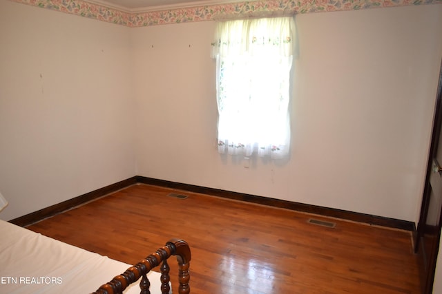 empty room with wood finished floors, visible vents, and baseboards