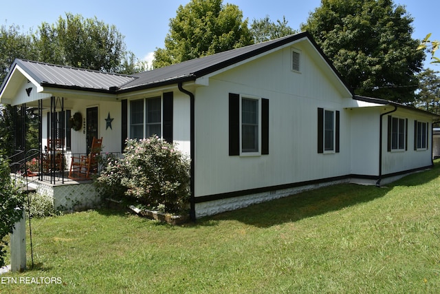 view of property exterior featuring covered porch, a yard, and metal roof