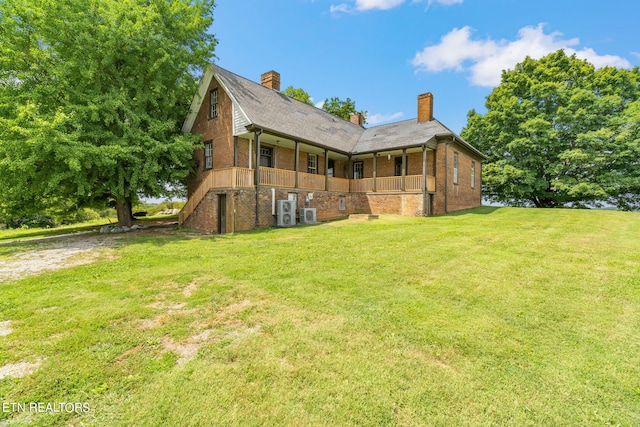 rear view of house featuring a yard, brick siding, a porch, and a chimney