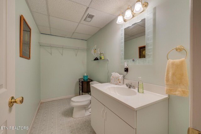 bathroom with tile patterned flooring, vanity, toilet, and a drop ceiling