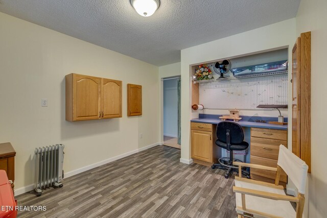 office space featuring built in desk, hardwood / wood-style flooring, radiator heating unit, and a textured ceiling