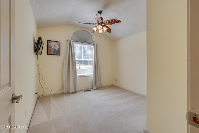 spare room featuring carpet floors, lofted ceiling, visible vents, a ceiling fan, and a textured ceiling