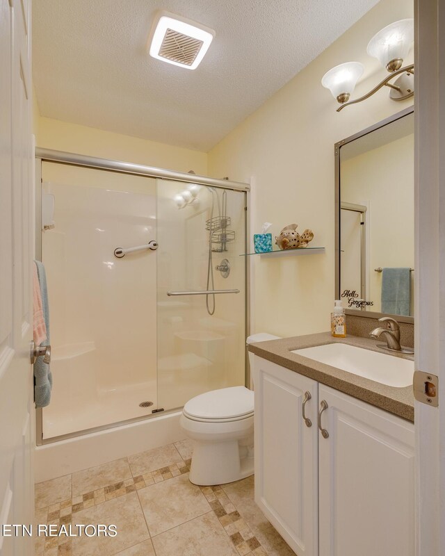 bathroom with a shower with door, vanity, a textured ceiling, tile patterned flooring, and toilet