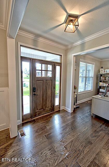 entryway with a textured ceiling, dark wood-type flooring, visible vents, baseboards, and ornamental molding