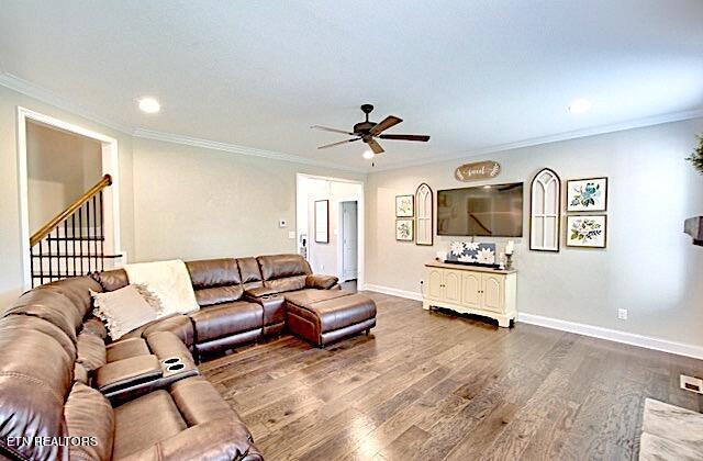 living room featuring dark wood-style floors, a ceiling fan, baseboards, and crown molding