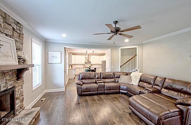 living room featuring crown molding, a fireplace, dark wood-style flooring, and stairs