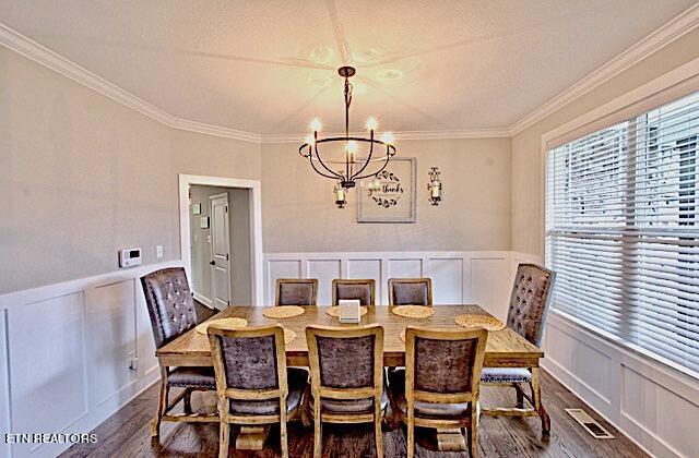 dining area featuring dark wood-style floors, ornamental molding, a decorative wall, and an inviting chandelier