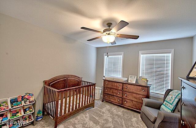 bedroom with light colored carpet, ceiling fan, and a crib