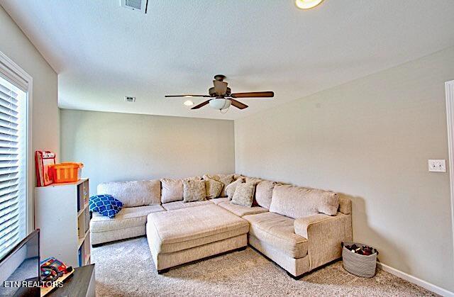 carpeted living room featuring baseboards, visible vents, and a ceiling fan