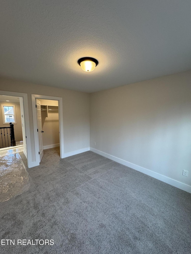 unfurnished bedroom featuring a spacious closet, a closet, a textured ceiling, and carpet flooring