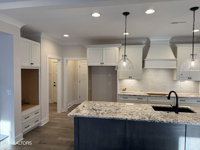 kitchen with premium range hood, pendant lighting, white cabinetry, sink, and light stone countertops