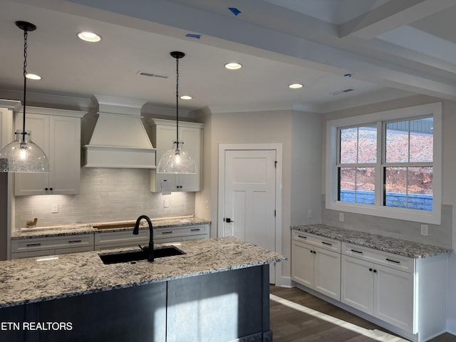 kitchen featuring hanging light fixtures, premium range hood, sink, and white cabinetry