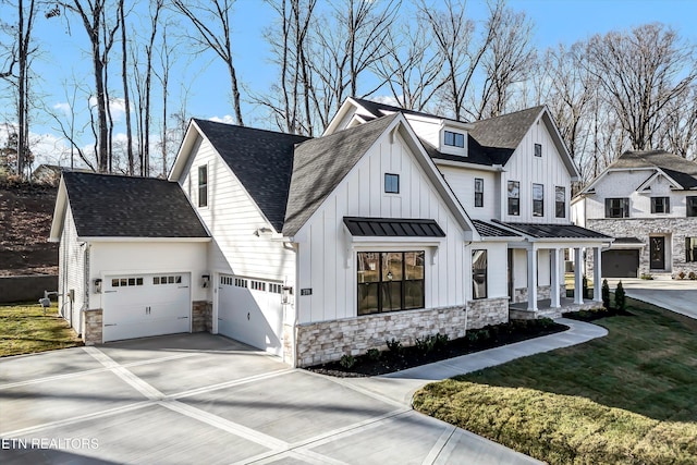 view of front of property featuring driveway, roof with shingles, an attached garage, stone siding, and board and batten siding