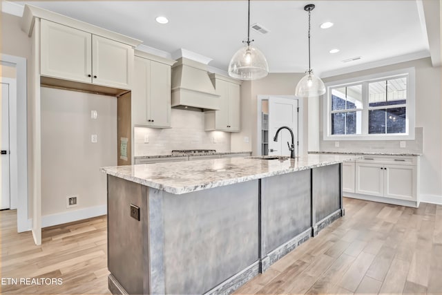 kitchen featuring light stone countertops, visible vents, premium range hood, a sink, and light wood-type flooring