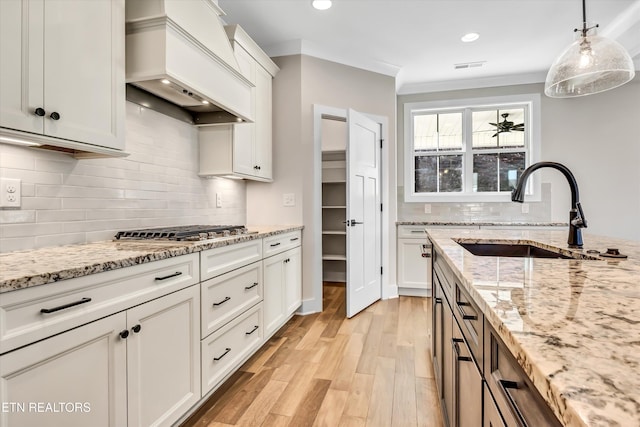 kitchen featuring stainless steel gas cooktop, pendant lighting, light wood-type flooring, custom range hood, and a sink