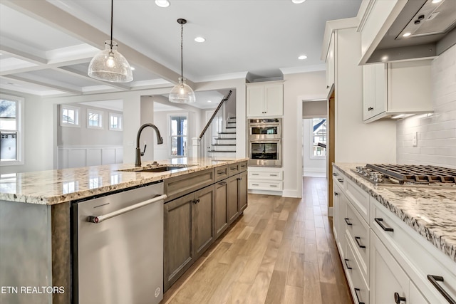 kitchen featuring light wood-style flooring, a sink, appliances with stainless steel finishes, wall chimney range hood, and tasteful backsplash