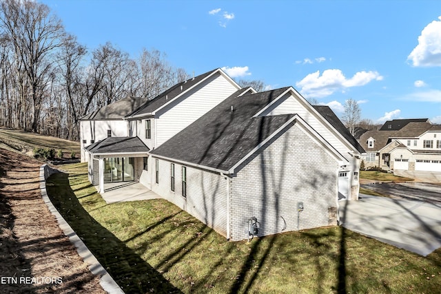 view of side of property featuring roof with shingles, an attached garage, a yard, concrete driveway, and brick siding