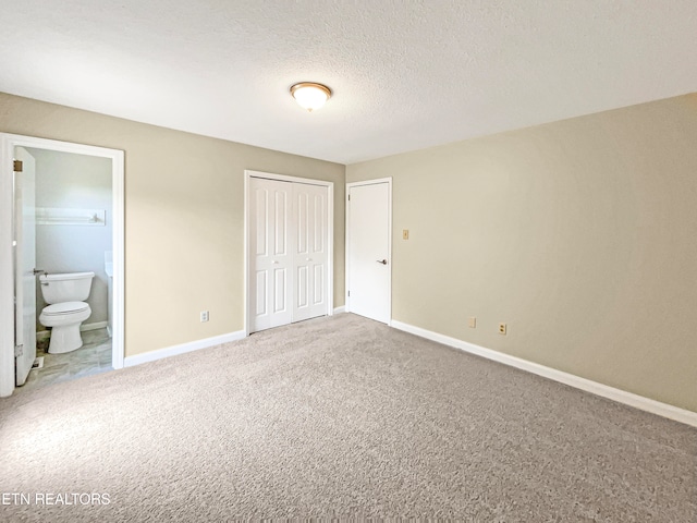 unfurnished bedroom featuring a textured ceiling, light carpet, and ensuite bath