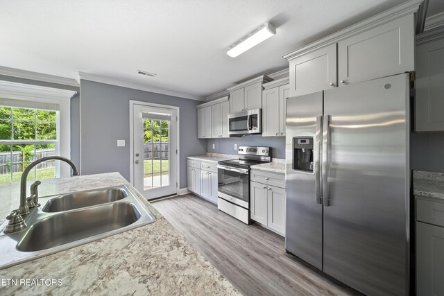 kitchen featuring sink, ornamental molding, light hardwood / wood-style floors, gray cabinetry, and stainless steel appliances