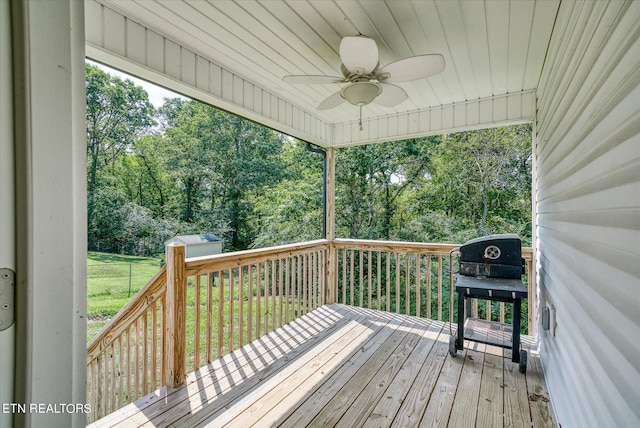 wooden terrace featuring a storage shed, a ceiling fan, an outbuilding, a grill, and fence