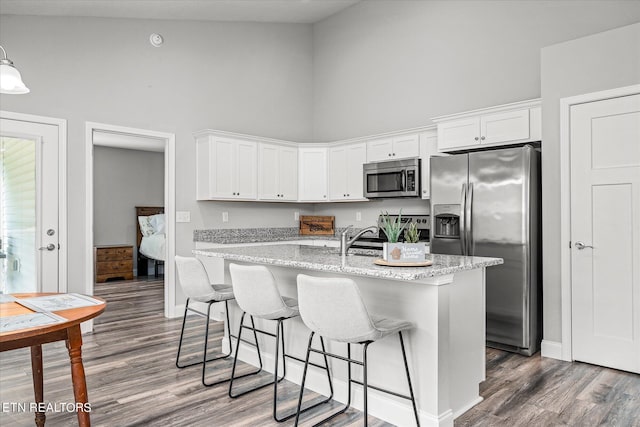 kitchen featuring appliances with stainless steel finishes, white cabinets, a center island with sink, and a high ceiling