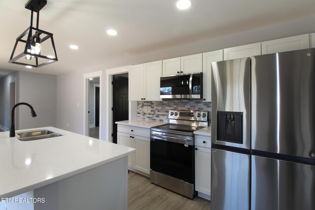 kitchen with sink, appliances with stainless steel finishes, light hardwood / wood-style flooring, decorative backsplash, and pendant lighting