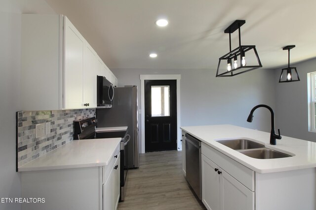 kitchen with white cabinetry, appliances with stainless steel finishes, light hardwood / wood-style floors, sink, and decorative light fixtures