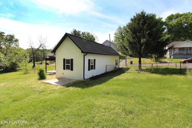 view of side of property featuring a shingled roof, a lawn, and fence